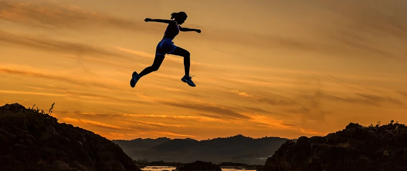 girl jumping across mountains at suset